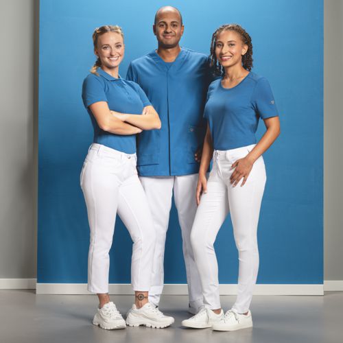 Een zorgteam van drie personen draagt witte werkbroeken en lichtblauwe tunieken.